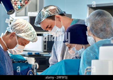 Porträt von Chirurgen, die sich während komplexer Operationen in einem sterilen Operationssaal über den Patienten lehnen. Ärzte sind fokussiert und äußerst aufmerksam. P Stockfoto