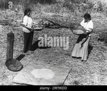 Kalifornien: ca. 1930 zwei kalifornische Indianerfrauen gewinnen Weizen, um die Körner von der Spreu zu trennen. Stockfoto