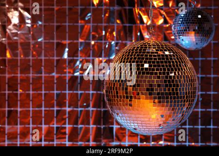 Glänzende Disco-Bälle an einem Partyvorhang unter farbigen Lichtern, Platz für Text Stockfoto