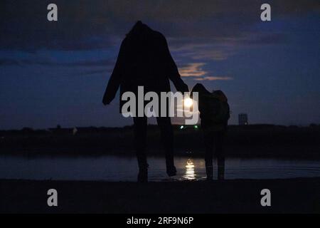 Berlin, Deutschland. 01. Aug. 2023. Eine Frau steht mit ihrem Kind am Abend vor einer Pfütze auf dem Tempelhofer Feld und beobachtet den Vollmond. Kredit: Carsten Koall/dpa/Alamy Live News Stockfoto