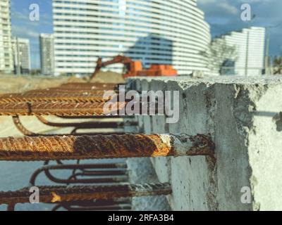 Betonblock mit rostigem Bewehrungsstahl, der innen herausragt. Befestigungselemente für den Bau von Betonhochhäusern. Bausteine im Hintergrund eines Hochhauses Stockfoto