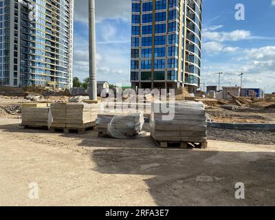 Baumaterialien, Pflasterplatten und Bordsteine liegen vor modernen Neubauten auf der Baustelle einer Großstadt. Stockfoto