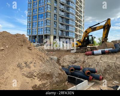 Bagger graben die Gräben auf einer Baustelle. Graben für die Verlegung von externen Kanalrohren. Abwasserentwässerungssystem für ein mehrstöckiges Gebäude. Graben Stockfoto