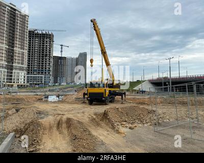 Großer gelber Mobilitätskran im modernen Industriebau, der auf einem Lkw montiert ist, wird beim Bau von neuen Wohnungen, Häusern, Gebäuden in einem großen C verwendet Stockfoto