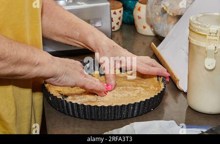 Der Koch bereitet die Basis für den Kuchen zu, den Teig in runder Metallform. Stockfoto