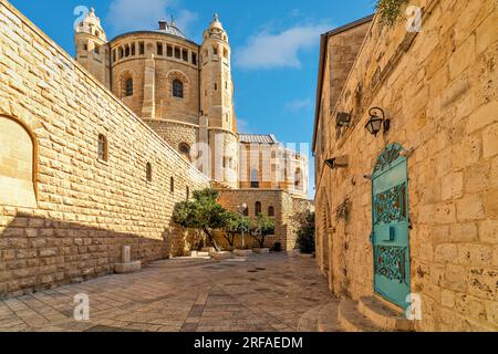 Blick auf die schmale Straße inmitten der alten Mauern wie die Dormition Abbey unter blauem Himmel im Hintergrund in der Altstadt von Jerusalem, Israel. Stockfoto