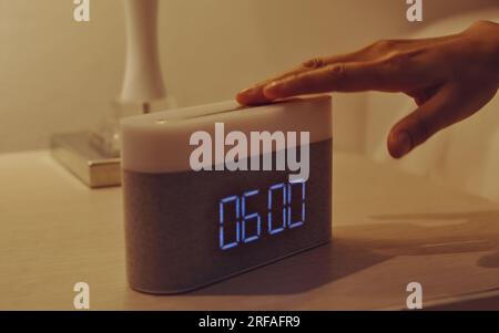 Die Hand einer jungen Frau schaltet den digitalen Wecker auf dem Nachttisch im Schlafzimmer zu Hause aus. Stockfoto