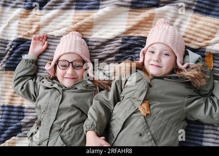 Zwei glückliche Zwillingsschwestern liegen auf einer Decke in einem Herbstpark. Die Mädchen lächeln und schauen in die Kamera. Draufsicht Stockfoto