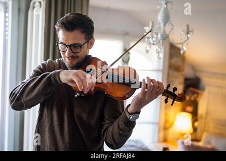 Junger weißer Mann, der zu Hause Geige spielt. Hobby Quality Time Happiness Konzept. Stockfoto