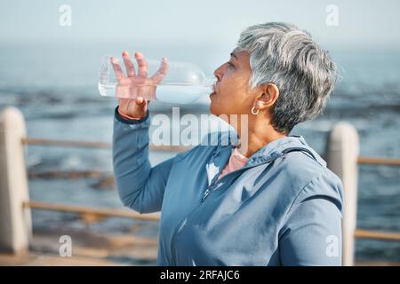 Draußen, Fitness oder Seniorin Trinkwasser für Hydratation, Wellness und Durst beim Strandlaufen, Training oder Sport. Flasche, Läufer oder ältere Menschen Stockfoto