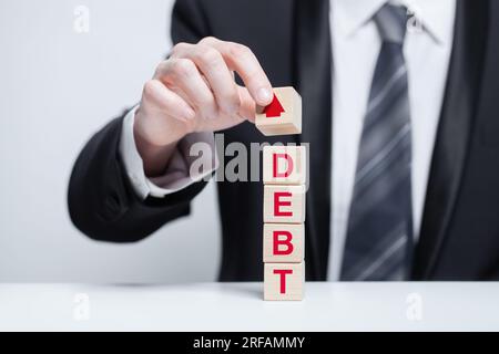 Holzblöcke mit Wortschulden und rotem Pfeil, Geschäftsmann mit Würfel. Geschäftskredit, Kredit, Hypothekenkonzept Stockfoto