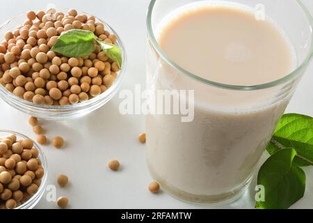 Detaildarstellung des alternativen Sojabrasses in Glas auf einem weißen Tisch mit Schüsseln voller trockener Samen. Erhöhte Aussicht. Stockfoto