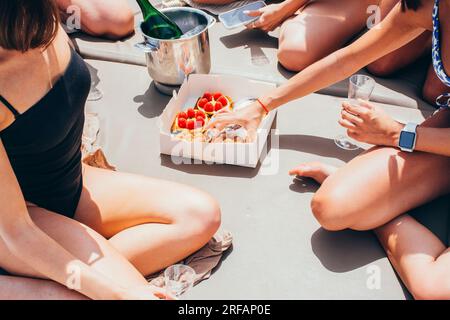 Eine Gruppe junger Frauen mit Champagner und Kuchen, die im Sommer auf einem Boot auf dem Meer segeln Stockfoto