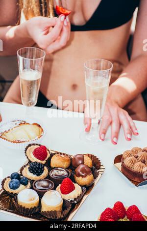 Eine Gruppe junger Frauen mit Champagner und Kuchen, die im Sommer auf einem Boot auf dem Meer segeln Stockfoto