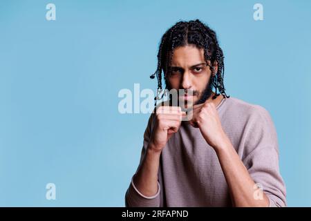 Ein starker arabischer Kämpfer, der in Boxposition steht, geballte Fäuste hat und in die Kamera schaut. Selbstbewusste Person, die eine Kampfposition mit einem Porträt mit ernstem Gesichtsausdruck zeigt Stockfoto