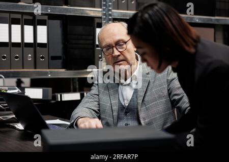 Professionelle Buchhalter belasten die Buchhaltung mit administrativen Unterlagen auf einem Laptop. Bürokratie Archivraum voll mit Ordnern und Diagrammen Stockfoto