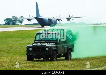 Rollendemonstration der britischen Streitkräfte. Militärischer Land Rover, der eine Rauchwand legte, nachdem er von einem RAF C-130 Hercules entladen wurde, der gerade startet Stockfoto