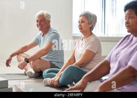 Gruppe von Personen, die auf Trainingsmatten sitzen und gemeinsam im Yoga-Studio trainieren Stockfoto