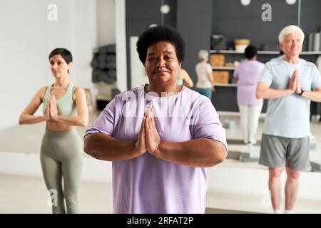 Porträt einer afroamerikanischen Frau, die zusammen mit Menschen im Fitnessclub meditiert Stockfoto