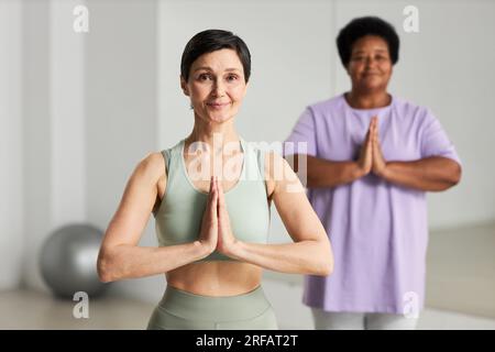 Porträt reifer Frauen, die in die Kamera schauen, während sie gemeinsam Yoga im Unterricht üben Stockfoto