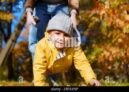 Ein glücklicher, lächelnder kleiner Junge in einer gelben Jacke, der Spaß beim Gehen auf seinen Händen hat. Vater hielt ihn an den Füßen. Hochwertiges Foto Stockfoto