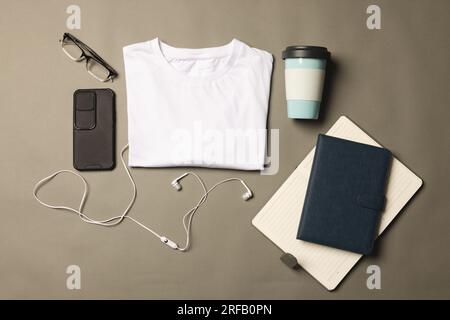 Flache Lagen aus weißem T-Shirt, Smartphone, Ohrhörern und Notizbüchern mit Kopierbereich auf grauem Hintergrund Stockfoto