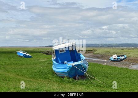 Es gibt drei blaue Boote, die alle am Sumpf am engen Fluss entlang Penclawdd am Anfang der Gower-Halbinsel festgemacht sind. Stockfoto