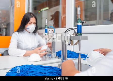 Das Mädchen arbeitet an der Maschine für die Herstellung von medizinischen Masken mit Nanofasern und löten die Schleifen mit Ultraschall an sie. Coronovirus und Covid- Stockfoto
