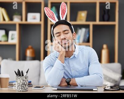 Müde, schlafend und ein Mann zu ostern in einem Büro mit Hasenohren zum Feiern oder gelangweilt von einer Party. Stress, Kaninchen und ein junger asiatischer Geschäftsmann Stockfoto