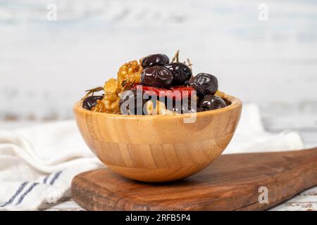 Gemischte Oliven mit schwarzen Oliven, Walnüssen, getrockneten Tomaten und Thymian in einer Holzschüssel. Oliven auf weißem Holzhintergrund. Mediterrane Küche. Veganes Essen Stockfoto