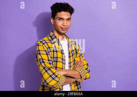 Porträt eines hübschen, netten Mannes mit stilvollen Ohrringen tragen ein kariertes Hemd, das die Arme auf violettem Hintergrund gekreuzt hält Stockfoto