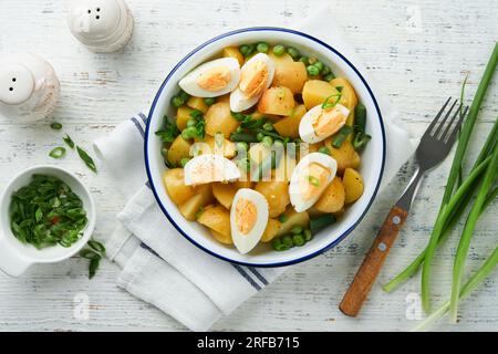 Traditioneller Kartoffelsalat mit Speck und Eiern in einer weißen Schüssel. Picknick-Food-Konzept. Schüssel mit warmem Kartoffelsalat. Deutscher Kartoffelsalat. Draufsicht. Stockfoto