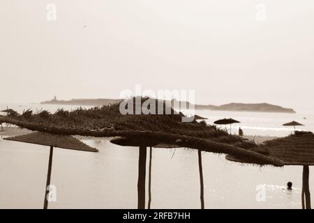 Strohschirme in Sepia-Tönen am Strand mit Blick auf das Meer. Stockfoto