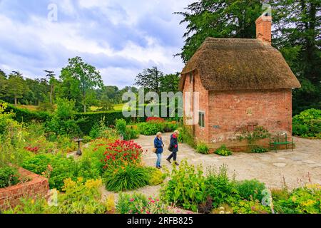 Ein kleines rotes Backsteingebäude mit Strohdach, umgeben von bunten Rändern im Cottage Garden im 'The Newt in Somerset', nr Bruton, England, Großbritannien Stockfoto