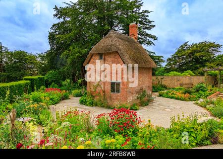 Ein kleines rotes Backsteingebäude mit Strohdach, umgeben von bunten Rändern im Cottage Garden im 'The Newt in Somerset', nr Bruton, England, Großbritannien Stockfoto