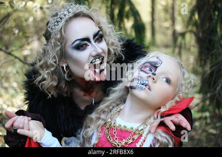 Eine Frau in Form eines Vampirs oder einer Zauberin beißt eine Prinzessin in märchenhaftem Make-up und mittelalterlichem Kleid. Bild für Halloween. Horizontales Foto Stockfoto