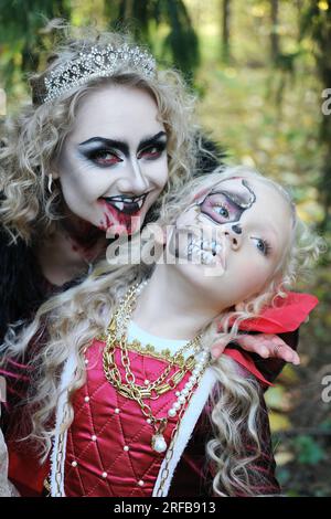 Eine Frau in Form eines Vampirs oder einer Zauberin lächelt und beißt eine Prinzessin in märchenhaftem Make-up und mittelalterlichem Kleid. Bild für Hallowe Stockfoto