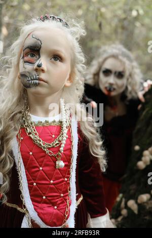 Eine Frau in Form eines Vampirs oder einer Zauberin beißt eine Prinzessin in märchenhaftem Make-up und mittelalterlichem Kleid. Die Hexe beobachtet den gi Stockfoto