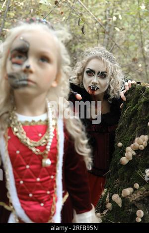 Eine Frau in Form eines Vampirs oder einer Zauberin beißt eine Prinzessin in märchenhaftem Make-up und mittelalterlichem Kleid. Die Hexe beobachtet den gi Stockfoto