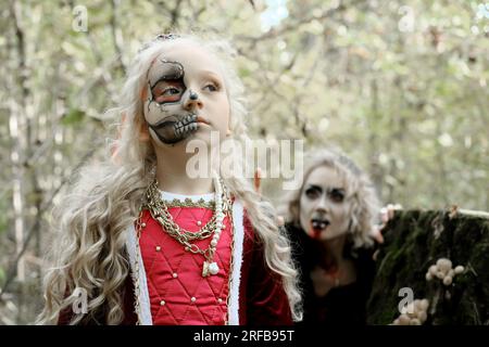 Eine Frau in Form eines Vampirs oder einer Zauberin beißt eine Prinzessin in märchenhaftem Make-up und mittelalterlichem Kleid. Die Hexe beobachtet den gi Stockfoto