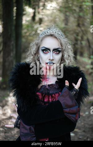 Eine Frau in Form eines Vampirs oder einer Hexe mit Make-up im Gesicht posiert für die Kamera im Wald. Vertikales Foto Stockfoto