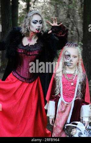 Eine Frau in Form eines Vampirs oder einer Zauberin beißt eine Prinzessin in märchenhaftem Make-up und mittelalterlichem Kleid. Halten Sie Ausschau nach Halloween. Mutter A. Stockfoto