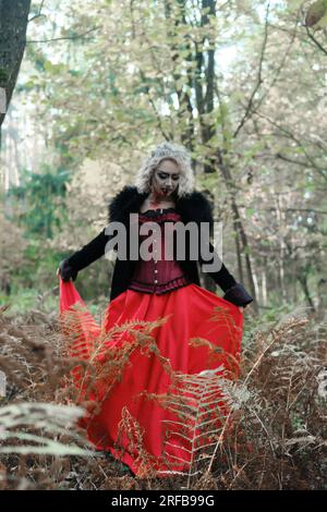 Eine Frau in Form eines Vampirs oder einer Hexe in einem mittelalterlichen Kleid wandert durch den Wald. Konzentrieren Sie sich auf Pflanzen. Vertikales Foto Stockfoto