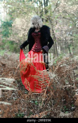 Eine Frau in Form eines Vampirs oder einer Hexe in einem mittelalterlichen Kleid wandert durch den Wald. Konzentrieren Sie sich auf Pflanzen. Vertikales Foto Stockfoto