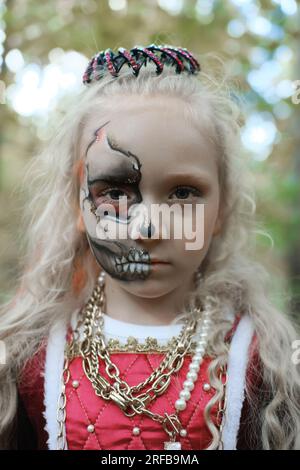 Ein Mädchen posiert im Wald in einem mittelalterlichen Kleid, wie eine tote Prinzessin mit Make-up im Gesicht. Ein Mädchen, das in die Kamera schaut. Vertikales Foto Stockfoto