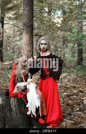 Eine Frau in Form eines Vampirs oder einer Zauberin und ein Mädchen in Form einer toten Prinzessin mit einer Skelettpuppe in der Hand Pose im Wald. Modus Stockfoto