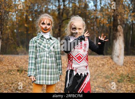 Ein Mädchen, verkleidet als Cheerleaderin, mit halbmassigem Skelett-Make-up und ihre Freundin mit Kürbis-Make-up. Lächelnde Mädchen, die in die Kamera schauen. Horizontal Stockfoto