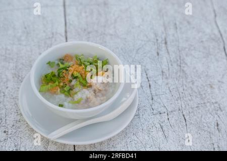 Gekochter Reis mit Schweinefleisch in weißer Schüssel auf weißem Holztisch Stockfoto