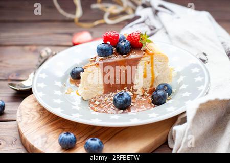 Scheibe Vanille-Käsekuchen mit gesalzener Karamellsauce, frischer Himbeere, Heidelbeere und Nüssen auf grauem Sternteller, Nahaufnahme Stockfoto