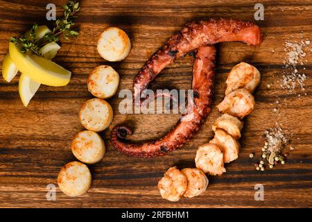 Gemischte gegrillte Meeresfrüchte auf Holzbrett, dunkler Hintergrund. Blick von oben. Stockfoto